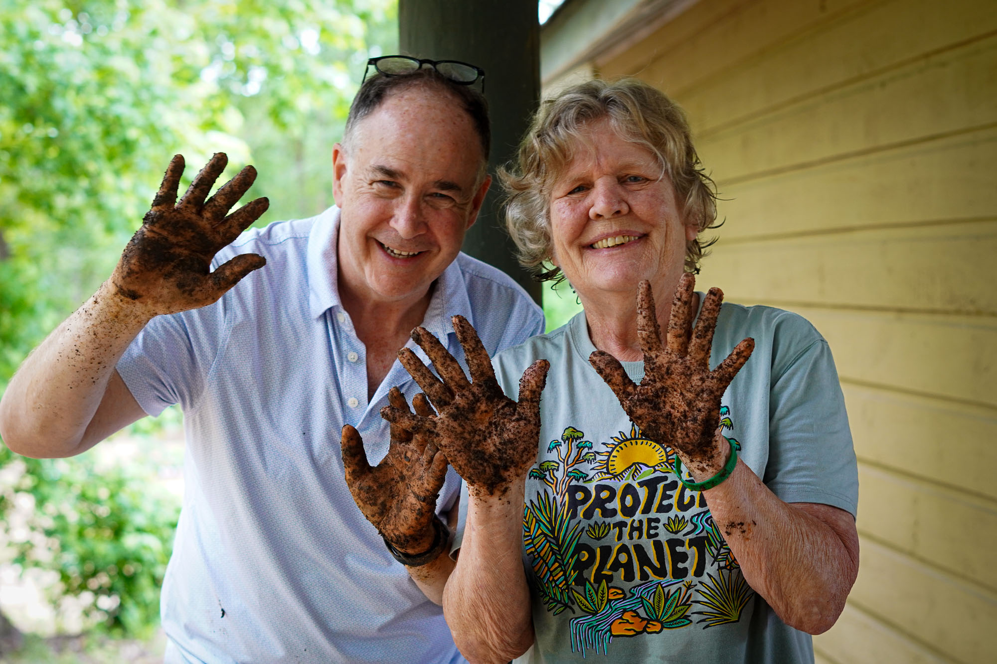A happy man and woman show off dirty hands from planting plants.